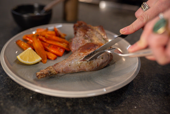 hands slicing into crane leg confit on a grey plate