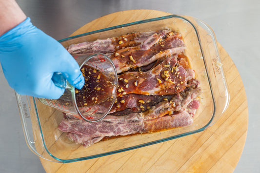 Pouring marinade over a baking dish of beef short ribs to make galbi