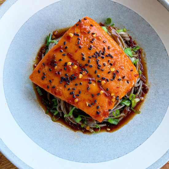 sous vide salmon topped with sesame seeds sitting on bowl of soba noodles in brown sauce