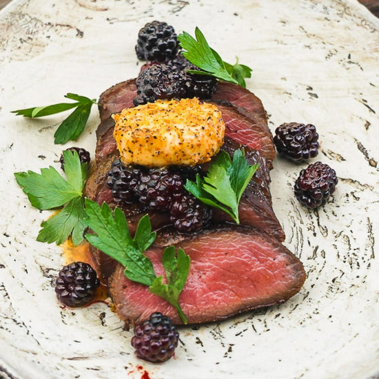 Sliced medium-rare venison strip loin topped with blackberries and compound butter