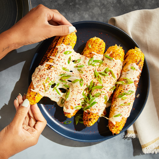 Woman pulling cheese-covered ear corn on the cob away from three more ears