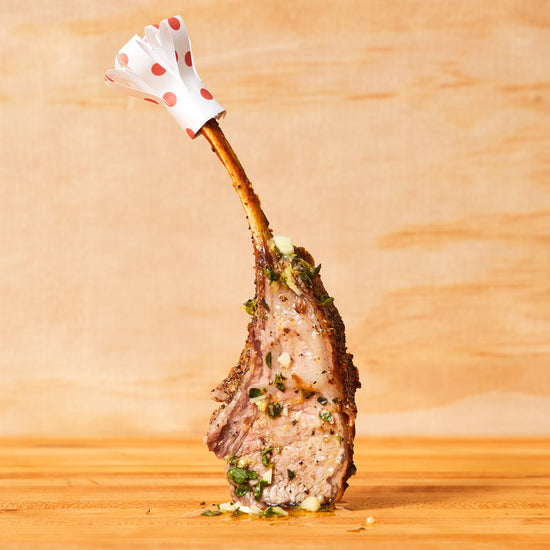 Slice of rack of lamb standing upright topped with herb sauce and a frilly bone cover