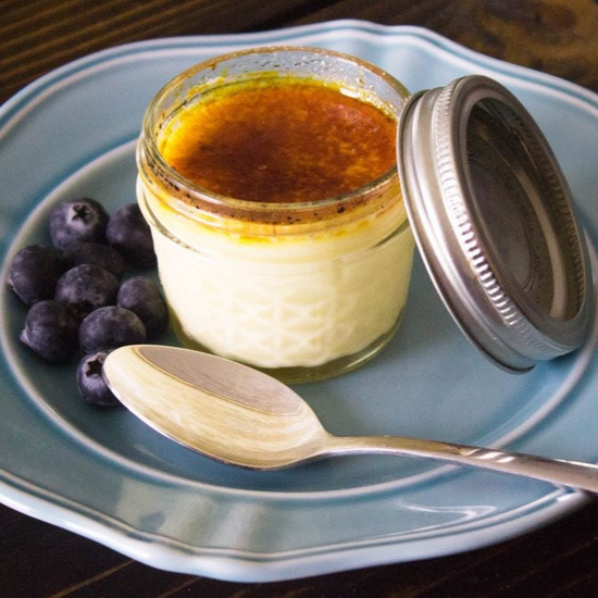 Creme brulee in a small canning jar set on a blue plate with blueberries on the side