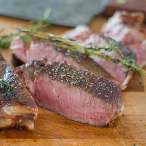 Sliced medium-rare ribeye steak on a cutting board topped with fresh thyme sprigs