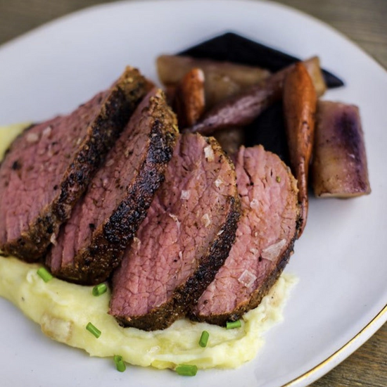 Sliced tri tip steak on a bed of mashed potatoes with roasted carrots on the side