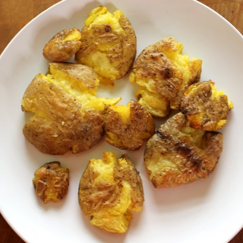 Smashed roasted yellow potatoes on a white plate