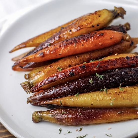 Plate of glazed whole rainbow carrots topped with fresh thyme