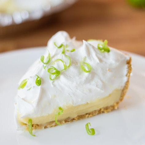 Slice of whipped cream-topped key lime pie on a white plate