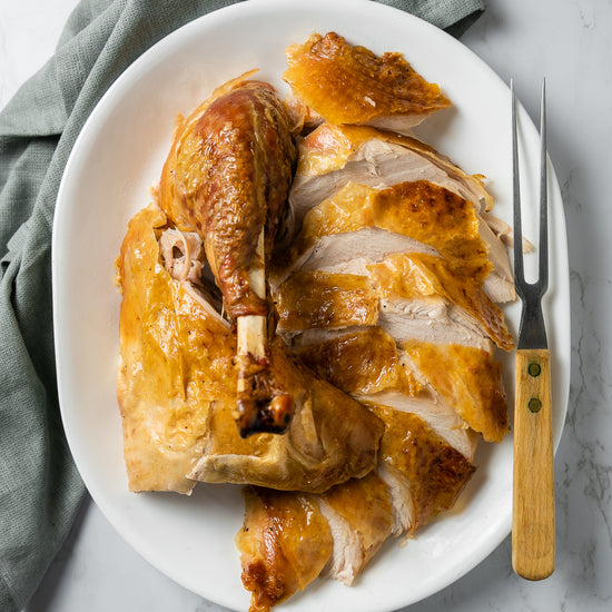 Sliced roast turkey pieces on a white platter with a carving fork