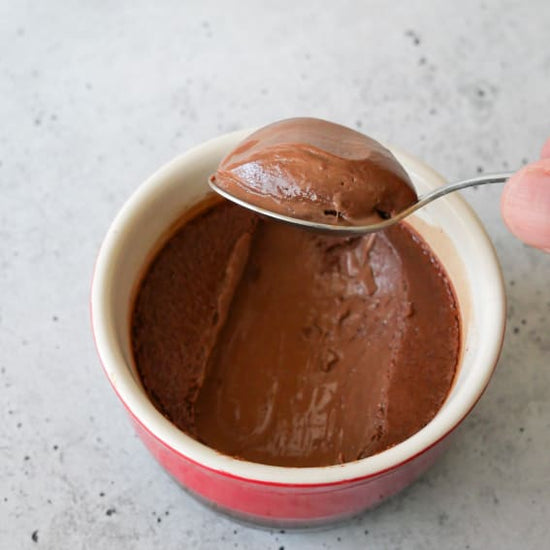 Spoon scooping up a bite of chocolate pot de creme from a red ramekin