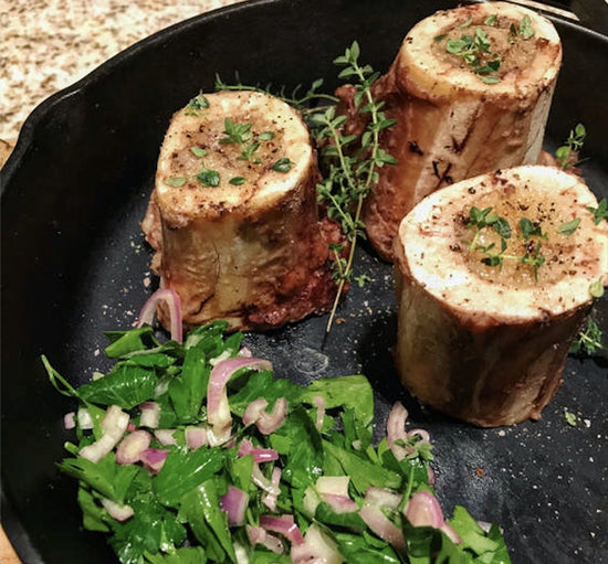 three servings of bone marrow on a black plate with parsley salad
