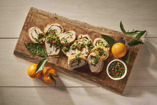 turkey breast roulade with chimichurri, sliced on a wood board with oranges