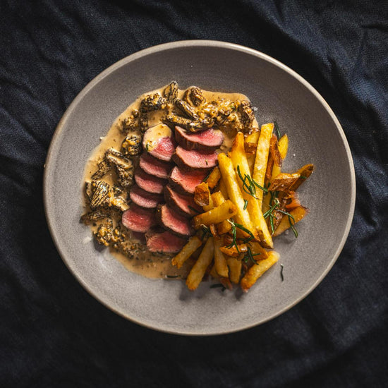 sliced venison loin with french fries and mushroom sauce on grey plate