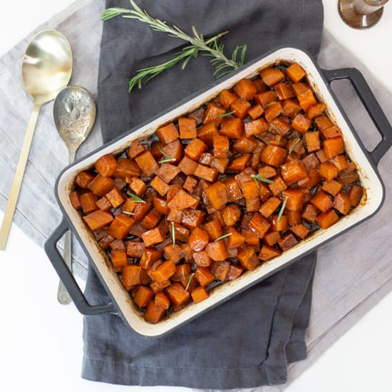 diced candied sweet potatoes in a baking dish garnished with rosemary