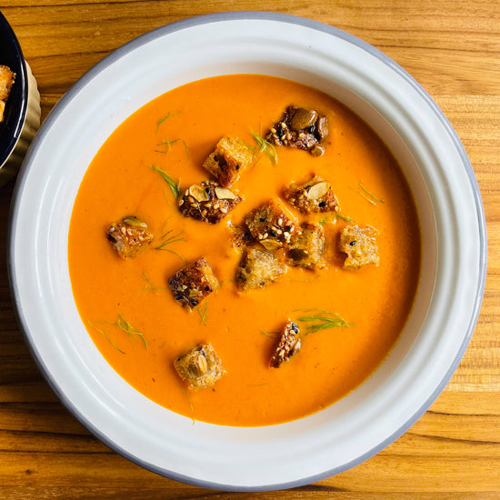 tomato soup in white bowl topped with croutons and dill fronds