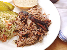 Sous vide barbecue pulled pork shoulder on a white plate with coleslaw and pickles on the side