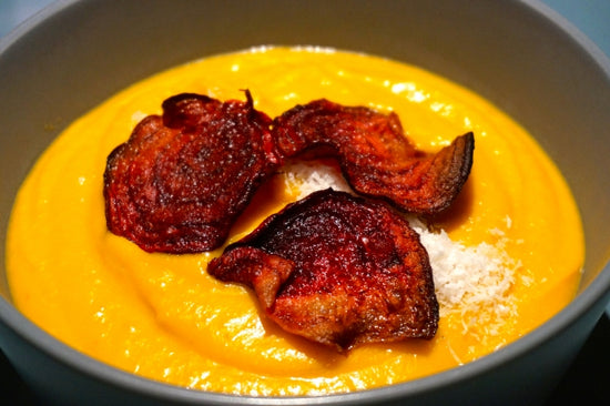 bowl of coconut pumpkin soup in black bowl topped with beet chips