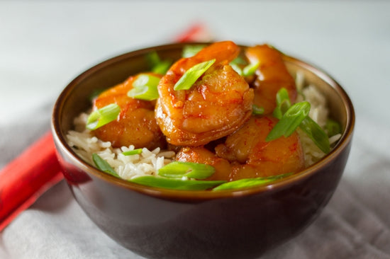 sous vide sriracha shrimp on a bed of rice in a brown bowl, topped with scallions