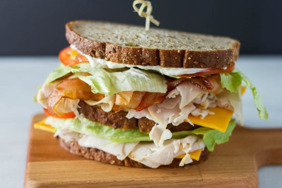turkey club sandwich on white bread on a wooden cutting board