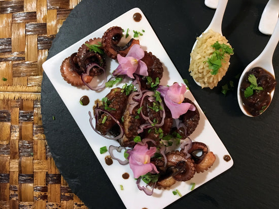 Trozos de pulpo cubiertos de mole con cebolla cruda y flores comestibles como guarnición