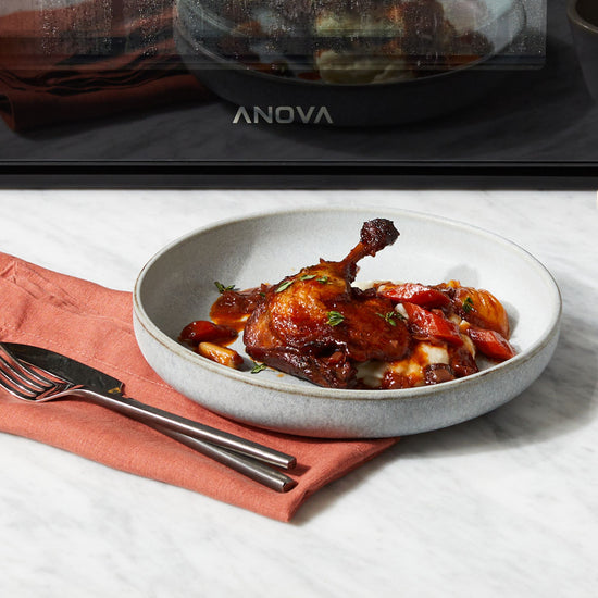 Steam braised duck legs with dried fruit on a grey plate in front of oven