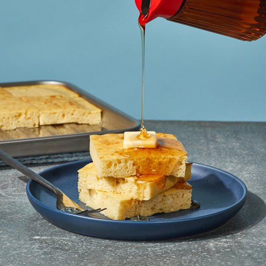 stack of square pancakes on a blue plate with syrup drizzling on top