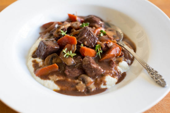 Beef bourguignon on top of mashed potatoes with gravy in a white bowl