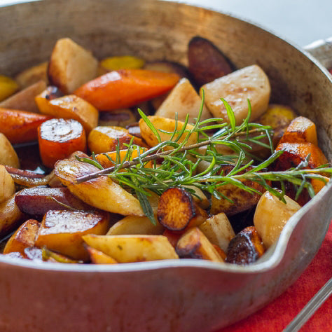 Mixed root vegetables in a saucepan topped with fresh rosemary