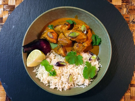 chicken curry in a green bowl served with rice, cilantro, and lime