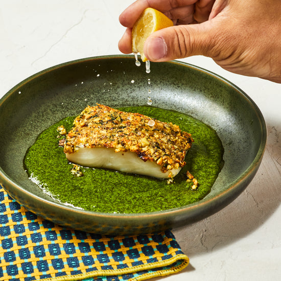 witte vis met een korst van noten en kruiden zittend op groene saus op een groen bord