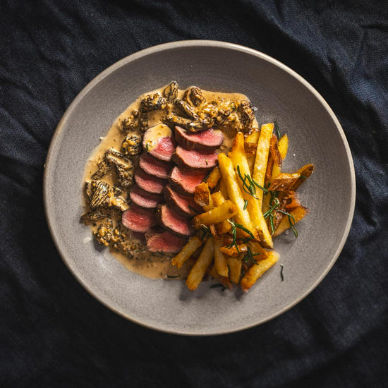 skivet hjortefilet med pommes frites og champignonsaus på grå tallerken