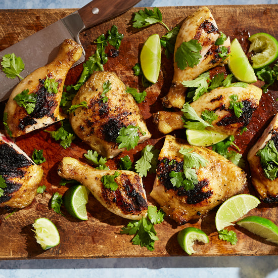 pernas de frango tailandês grelhadas numa tábua de cortar e cobertas com coentros e lima